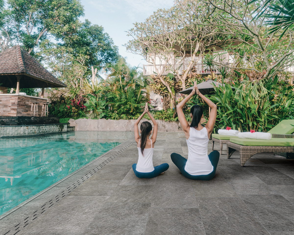 Mutter und Tochter machen Yoga neben einem Pool mit orientalischen Elementen